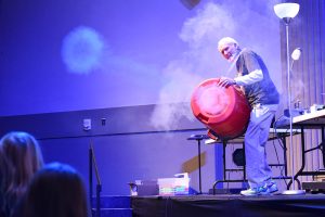 Glenn Govertsen on stage during one of his science shows for youth demonstrating an experiment.