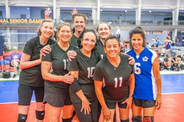 A women's volleyball team posing for a group photo on a court at the National Senior Games.