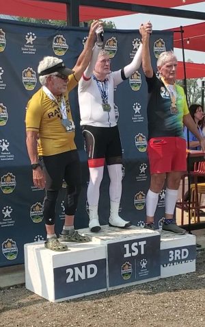 Three cyclists stand on a podium with their hands in the air.