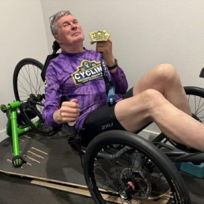 Jim DeGoey sits on his recumbent bike while holding the gold medal he won at the 2025 National Senior Games.