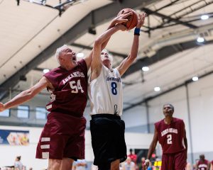 Two men leap in the air fighting for possession of a basketball during a game.