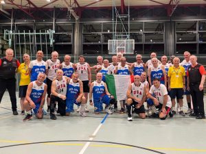 Two basketball teams of older men pose together. Some are wearing Team USA jerseys and others are wearing jersey's representing Italy.