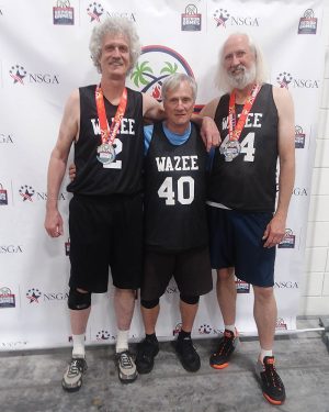 Three basketball teammates pose together in front of a branded backdrop at the 2022 National Senior Games.