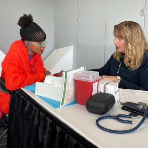 A health care provider shares information with an athlete. Both are sitting at a table and looking down like they are reading. Miscellaneous medical tools are on the table. 