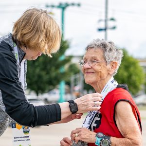 An older adult runner smiles proudly while receiving a medal at the 2025 National Senior Games.