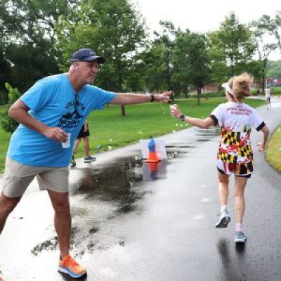 A volunteer hands a cup of water to a runner competing in the 10K road race at the 2025 National Senior Games.