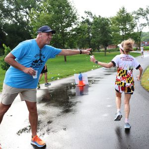 A volunteer hands a cup of water to a runner competing in the 10K road race at the 2025 National Senior Games.