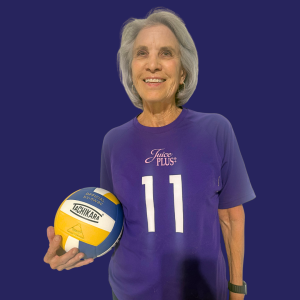 National Senior Games athlete Madelon Eichhorn stands smiling in a purple jersey and holding a volleyball.